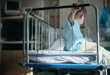 Hospitalizované trojročné dieťa na kovovej postieľke.